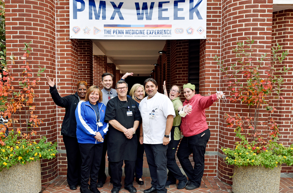 A group of Pennsylvania Hospital staff standing under a banner with PMX Week across the front. 